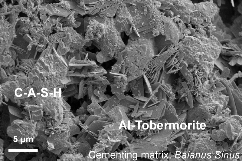 This microscopic image shows the lumpy calcium-aluminum-silicate-hydrate (C-A-S-H) binder material that forms when volcanic ash, lime and seawater mix. Platy crystals of Al-tobermorite have grown amongst the C-A-S-H in the cementing matrix. (Image: M. D. Jackson et al., 2017)